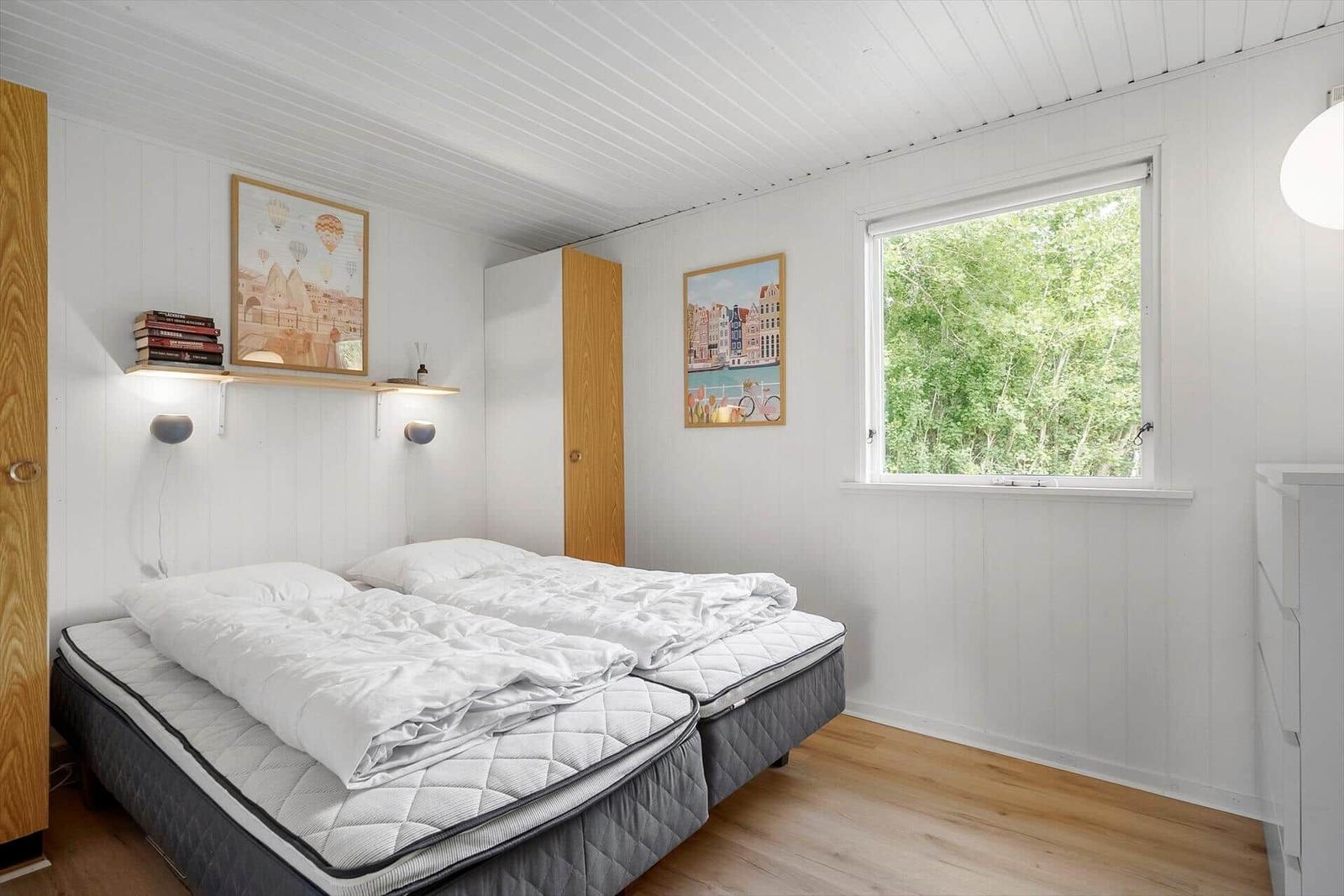 Zimmer mit Doppelbett, Fenster und Wandbildern.