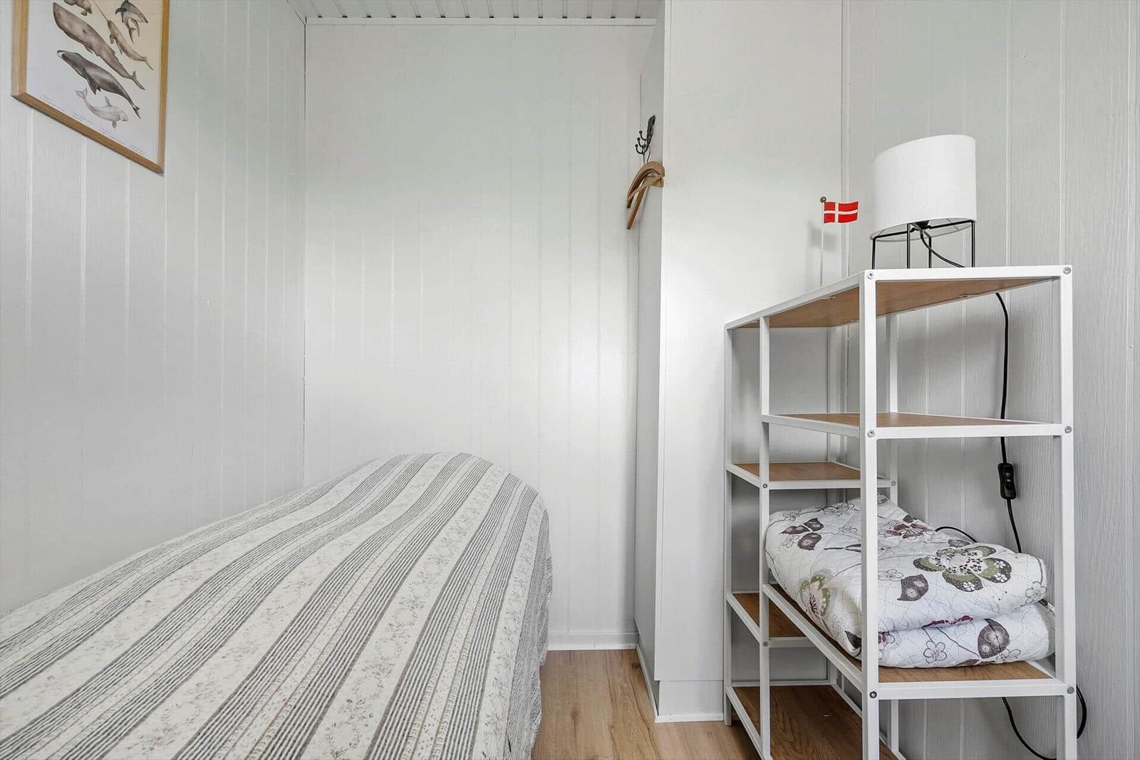 Schlafzimmer mit Bett und Regal. Daneben Flagge und Lampe.
