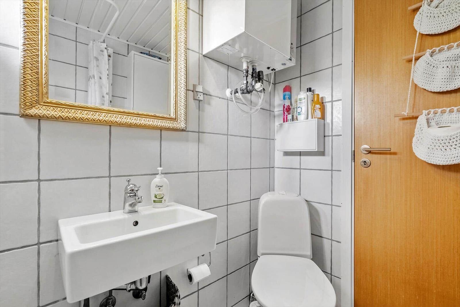 Badezimmer mit Waschbecken, Toilette und Spiegel mit goldenem Rahmen.