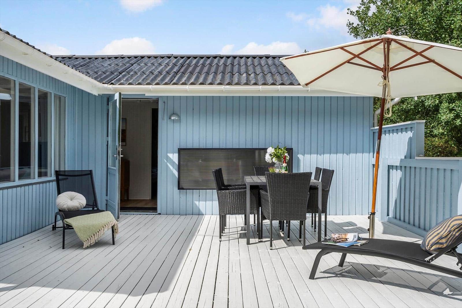 Terrasse mit Tisch, Stühlen, Liege und Sonnenschirm vor blauem Haus