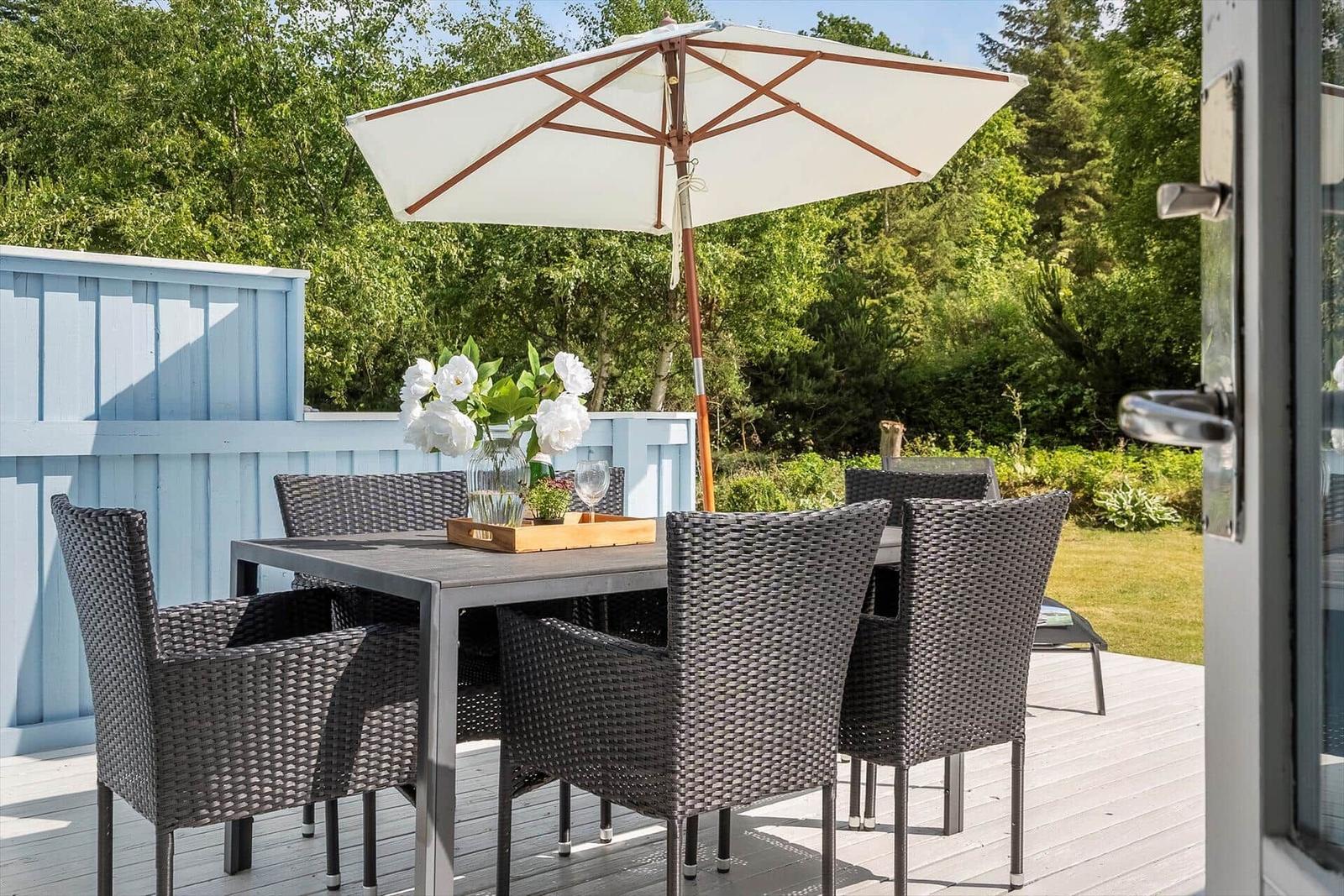Terrasse mit Tisch, Stühlen und Sonnenschirm. Hintergrund: grüner Garten und blaue Wand.