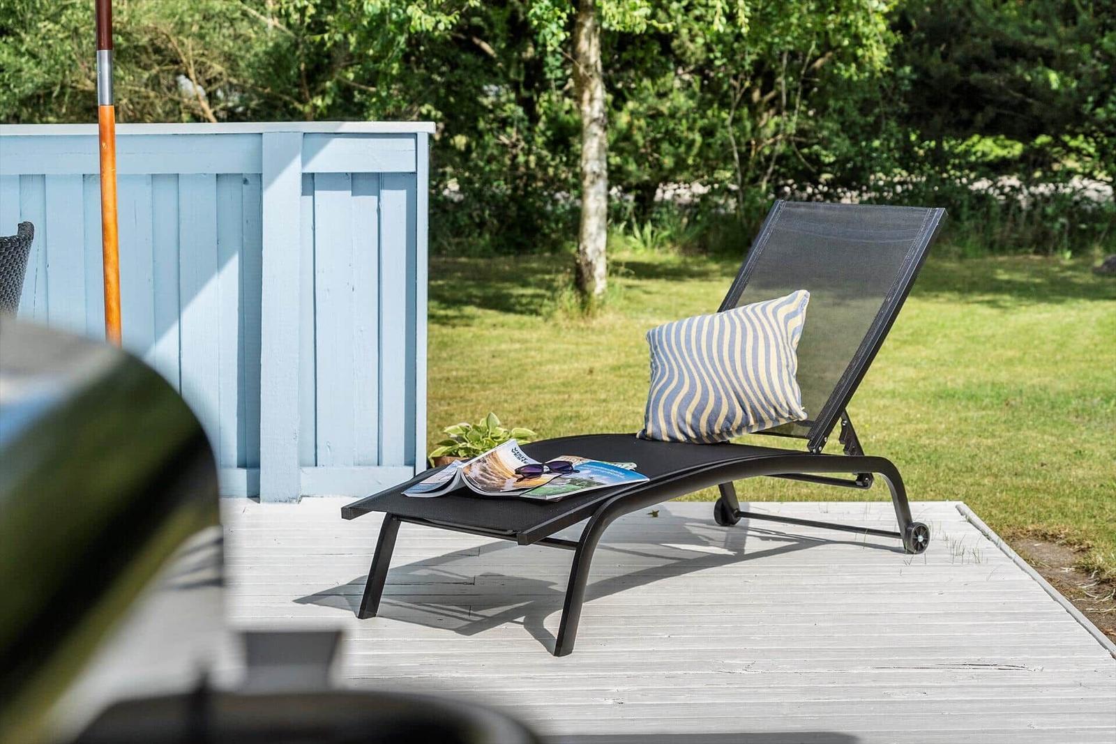 Schwarze Liegestuhl mit Kissen auf Terrasse neben blauem Holzzaun.