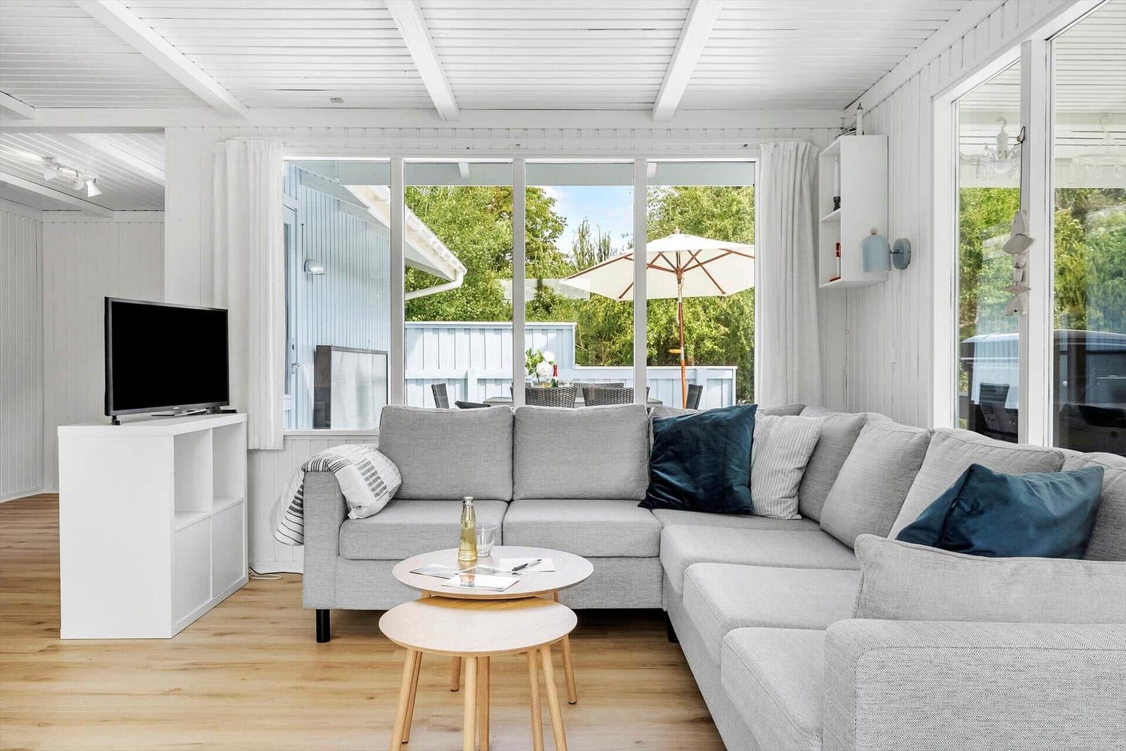 Wohnzimmer mit grauem Sofa, TV und großem Fenster zum Garten.