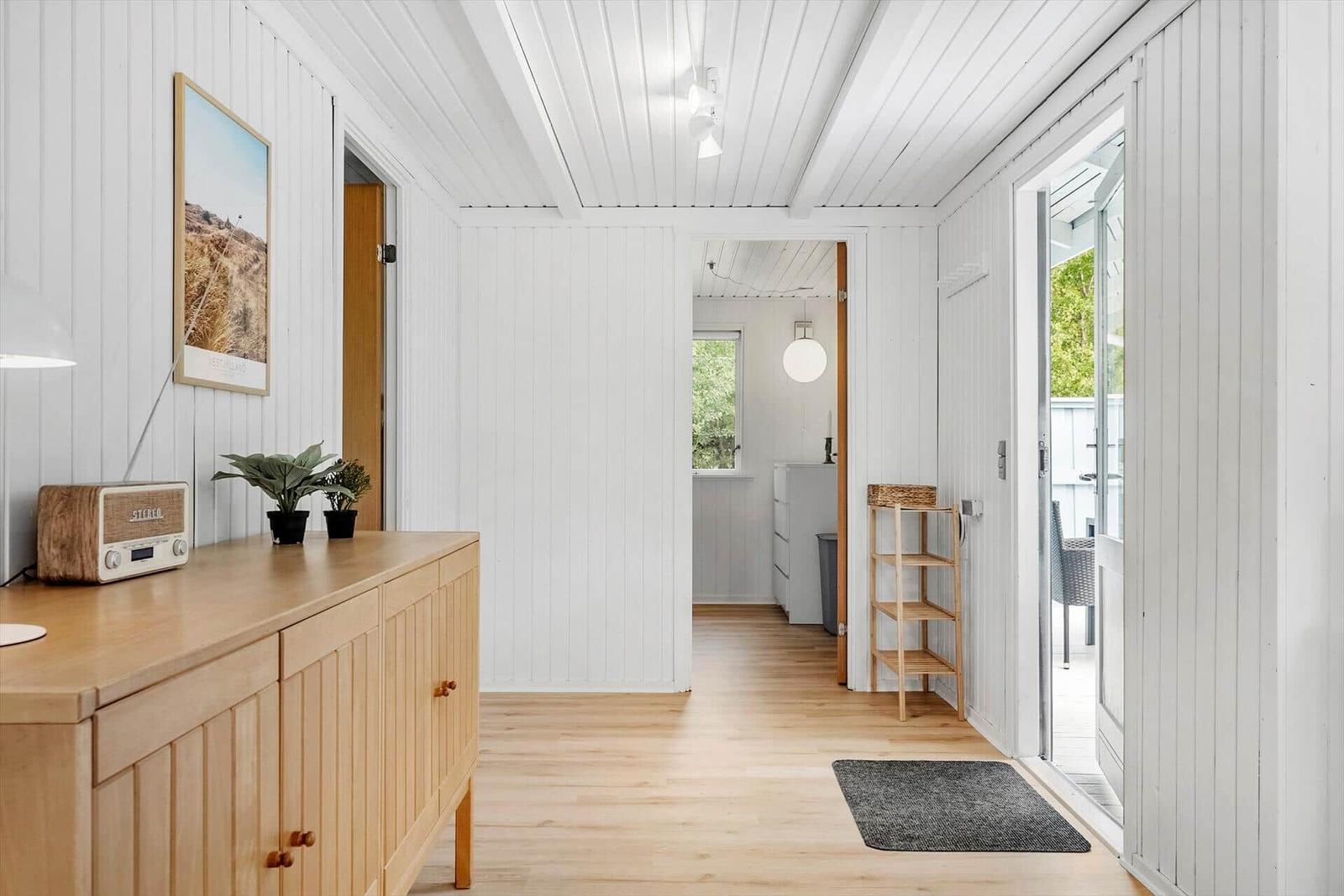 Haus mit Holzdielen und weißem Paneel, Eingangsbereich mit Schrank und Tür zu Balkon.