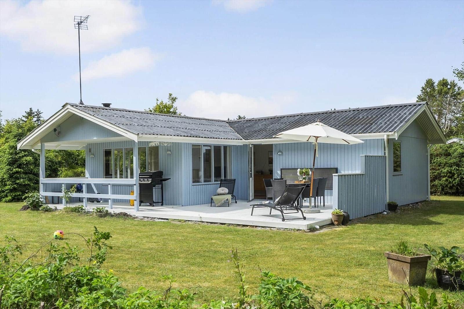 Ein hellblauer Ferienhaus mit Terrasse, Grill und Sitzgelegenheiten im Garten.