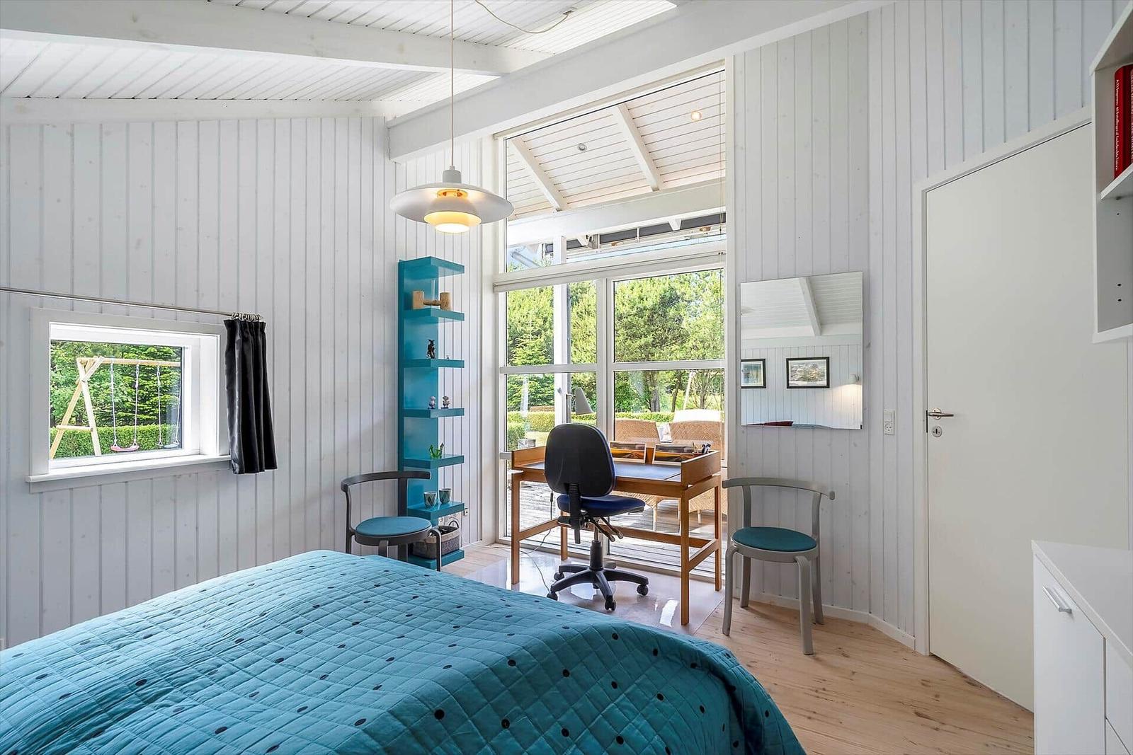 Schlafzimmer mit Bett, Schreibtisch und Blick auf Garten