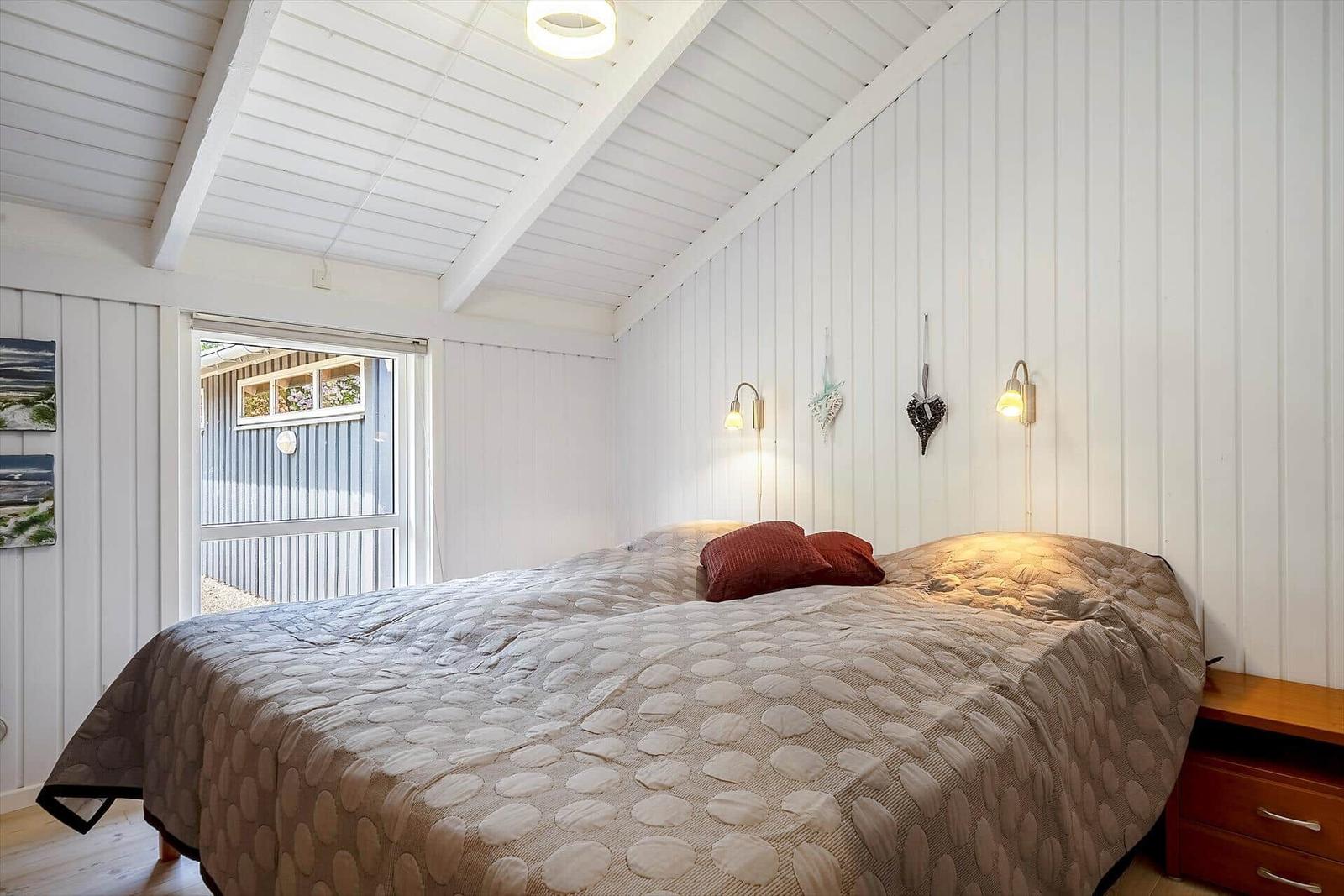 Schlafzimmer mit Bett, Nachttisch und Fenster zur Außenseite.