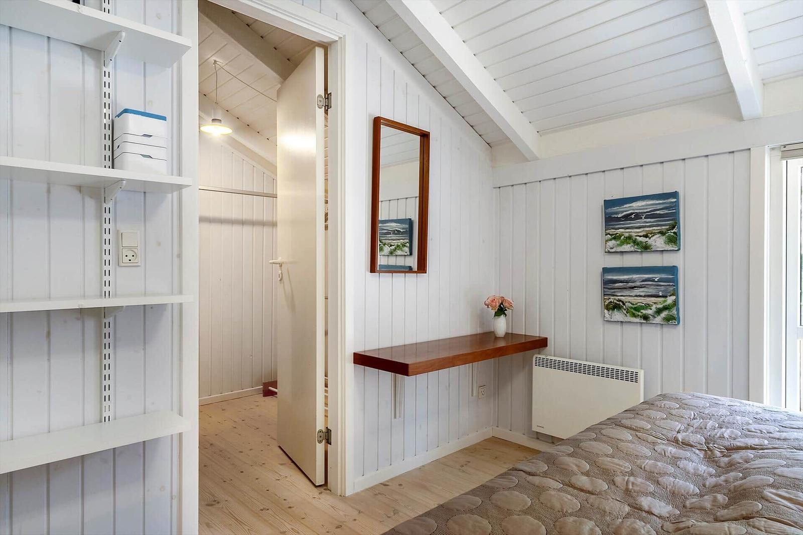 Schlafzimmer mit Bett, Wandregal, Spiegel und zwei Bildern an der Wand.