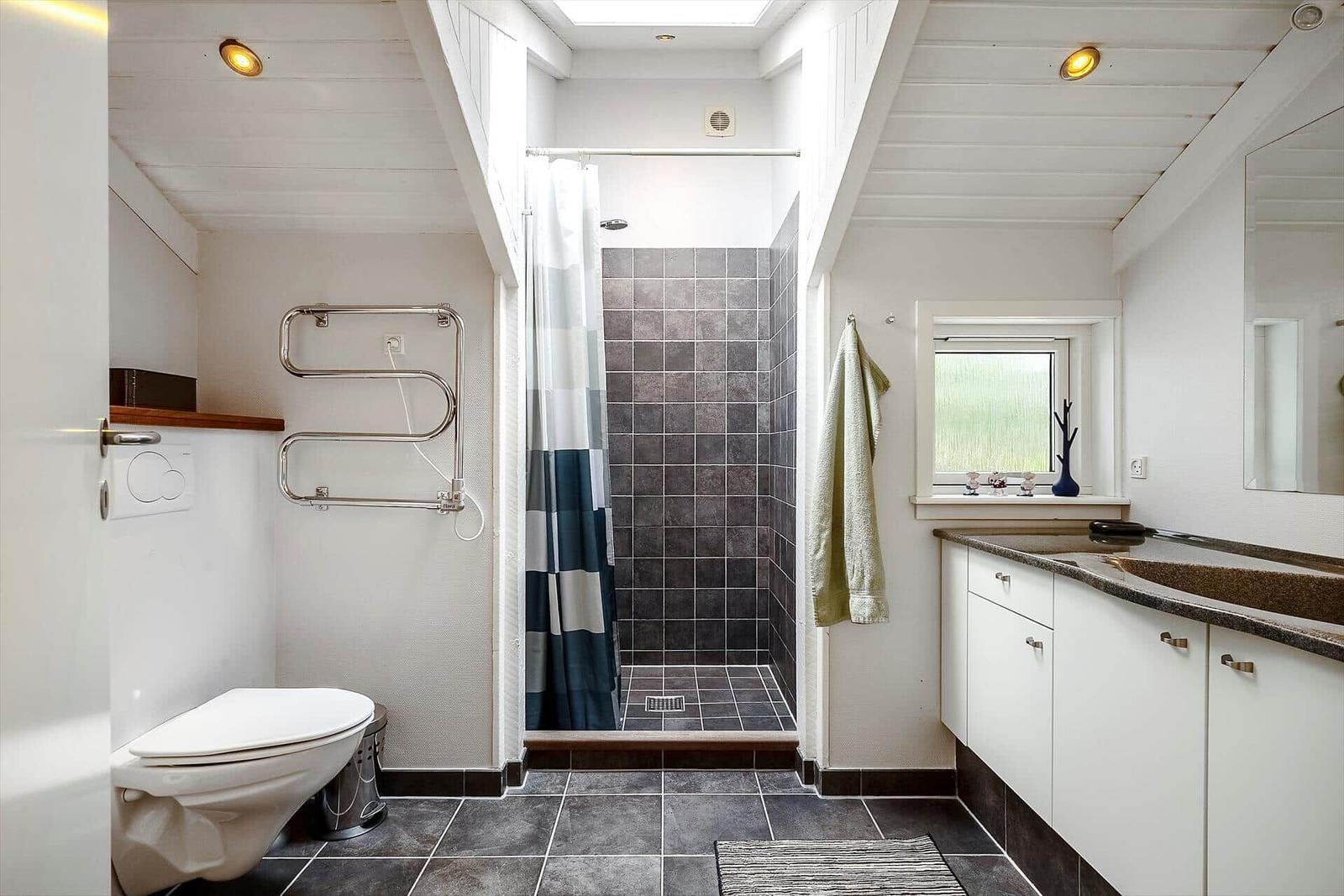 Badezimmer mit Dusche, Waschbecken und Toilette. Dunkle Fliesen und weißer Schrank.
