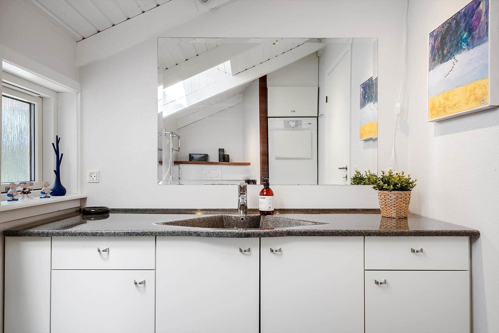 Waschbecken mit Spiegel, Fenster und Küchenzeile mit Arbeitsplatte.