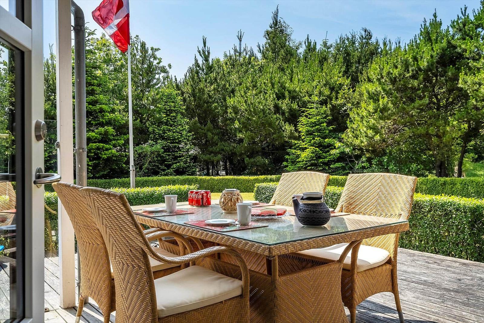 Terrasse mit Esstisch und Stühlen, umgeben von grünen Hecken und Bäumen.