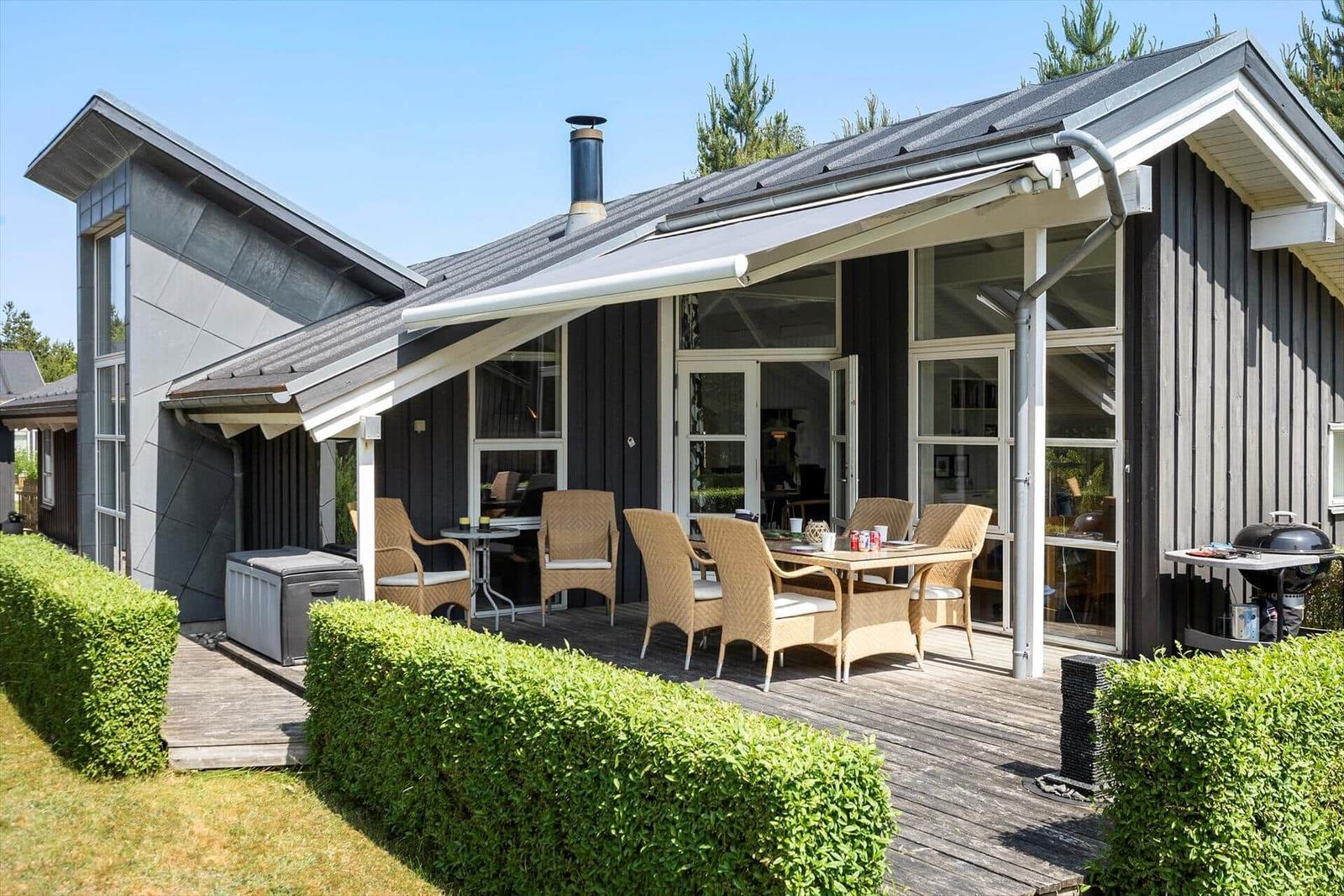 Terrasse mit Sitzgruppe, Grill und Whirlpool. Modernes Haus mit Holzfassade und Glasfront.