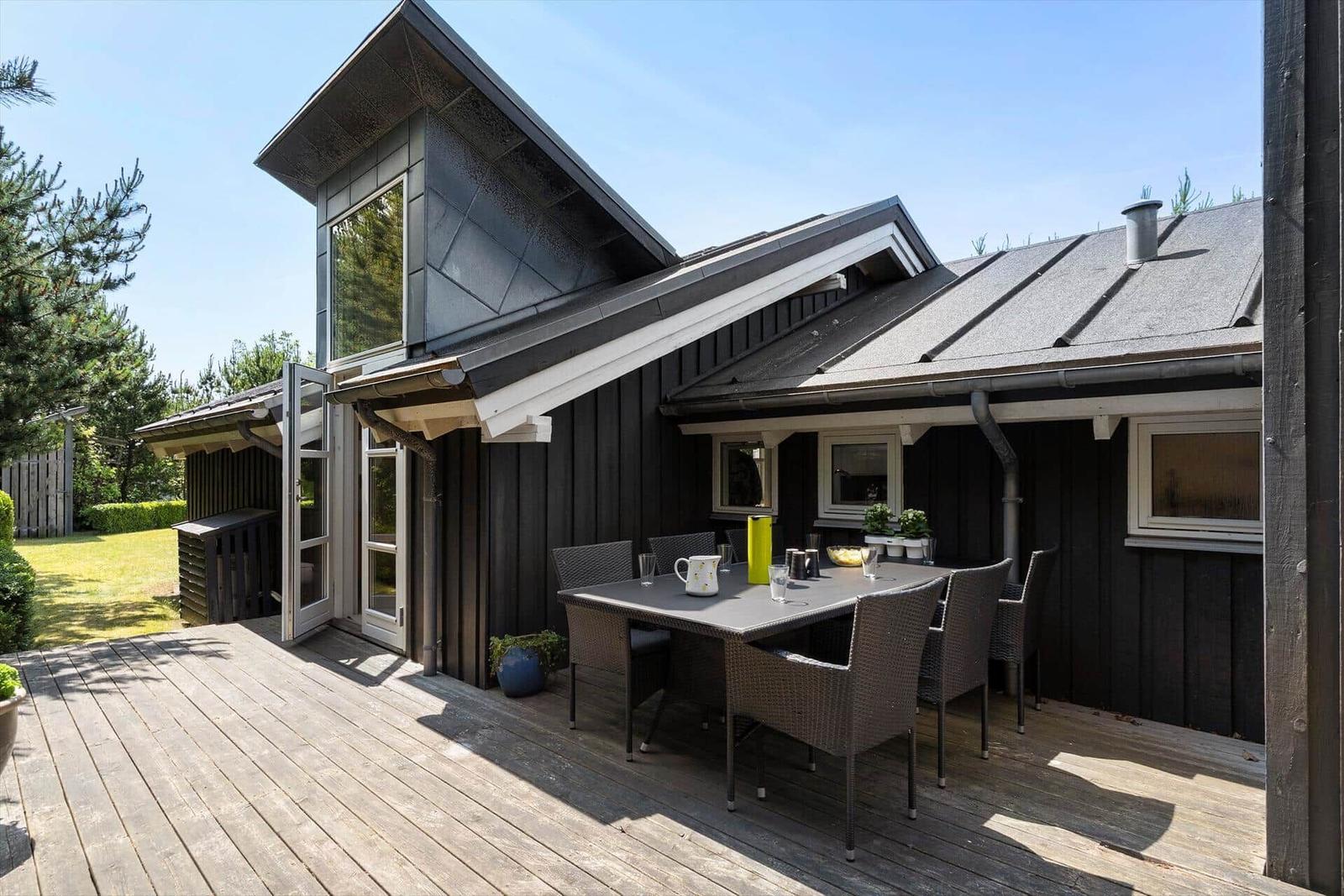 Terrasse mit Tisch und Stühlen vor einem Haus mit dunkler Fassade und Glasfront.
