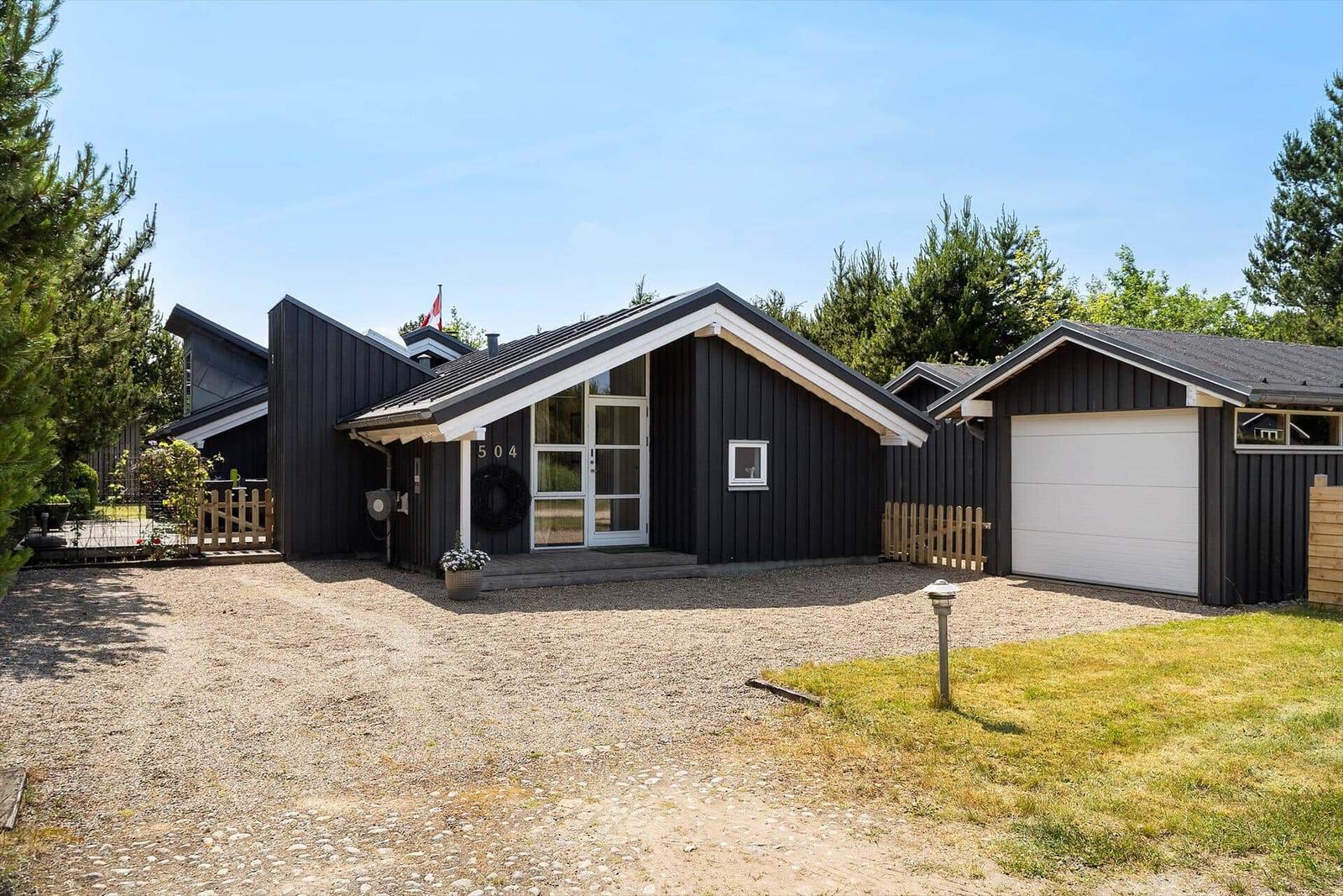 Schwarzes Holzhaus mit Garage und Vorgarten unter blauem Himmel.