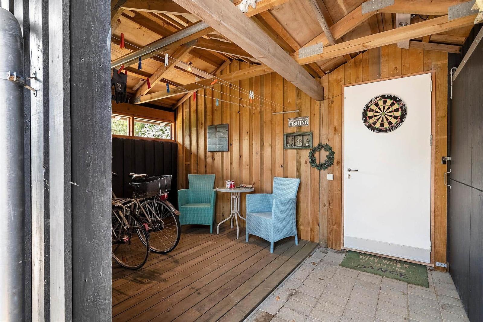 Holzveranda mit zwei blauen Stühlen, Tisch und Dartscheibe an der Tür.