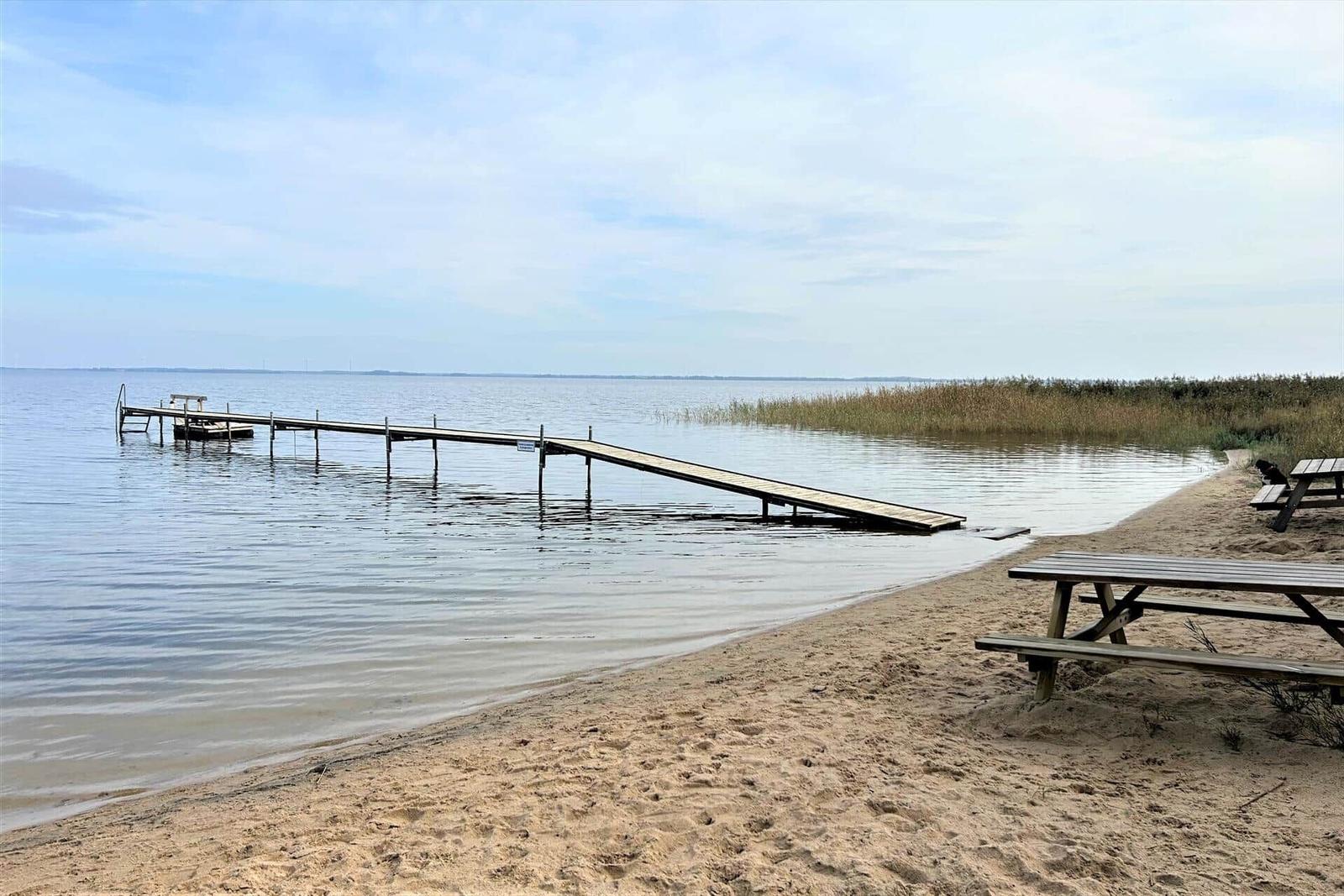 Holzsteg führt zu Wasser, Sandstrand mit Picknicktischen