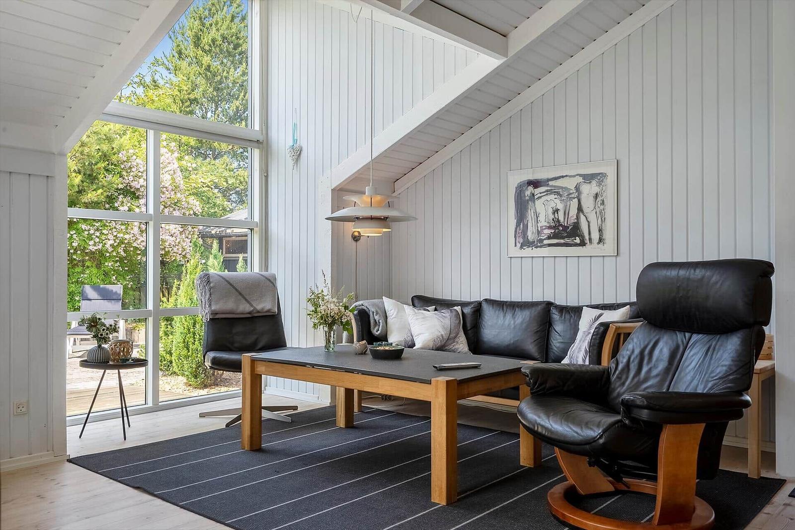 Wohnzimmer mit schwarzen Ledermöbeln, Holztisch und großem Fenster zur Außenterrasse.