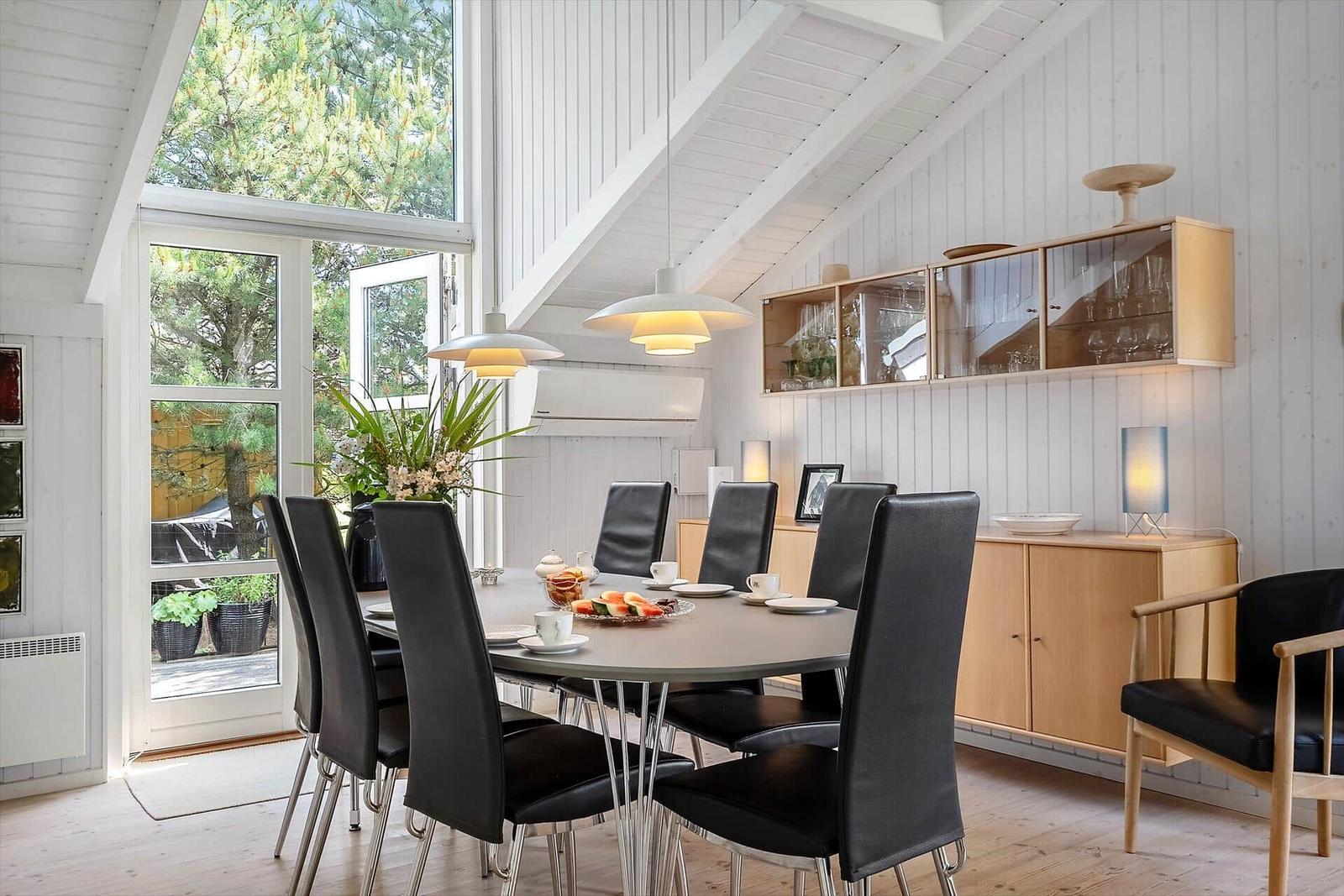 Esszimmer mit runder Tisch, schwarzen Stühlen und Holzmöbeln. Große Fenster und helle Wände.