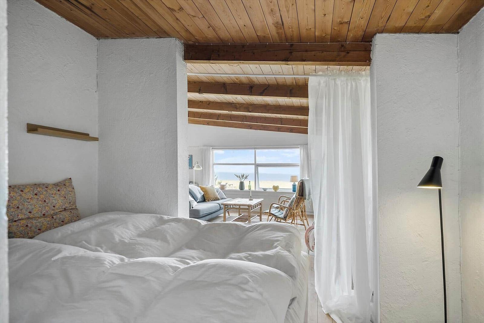 Bedroom with view to living room and beach. Wooden ceiling and white walls.