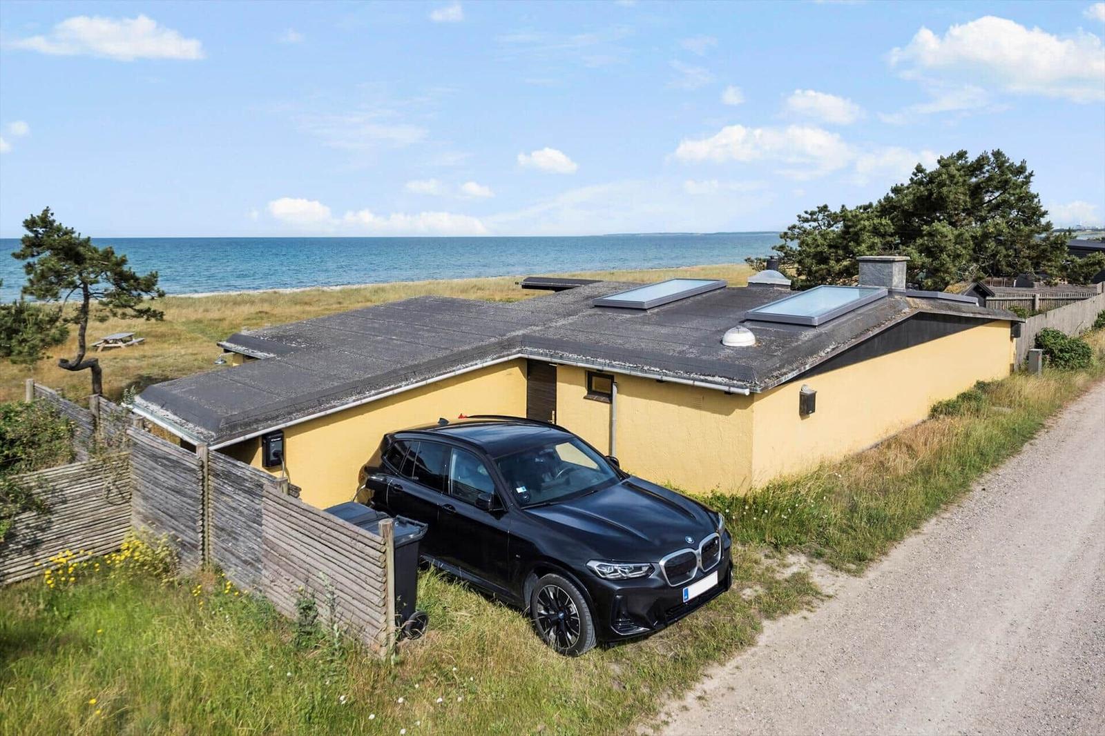 A yellow house with skylights stands by the beach. A black car is parked in front of the house.