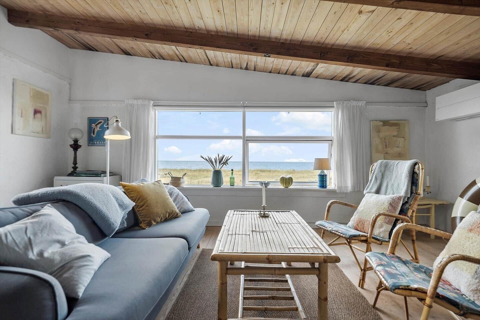 Living room with sofa, chairs, and sea view through large windows.