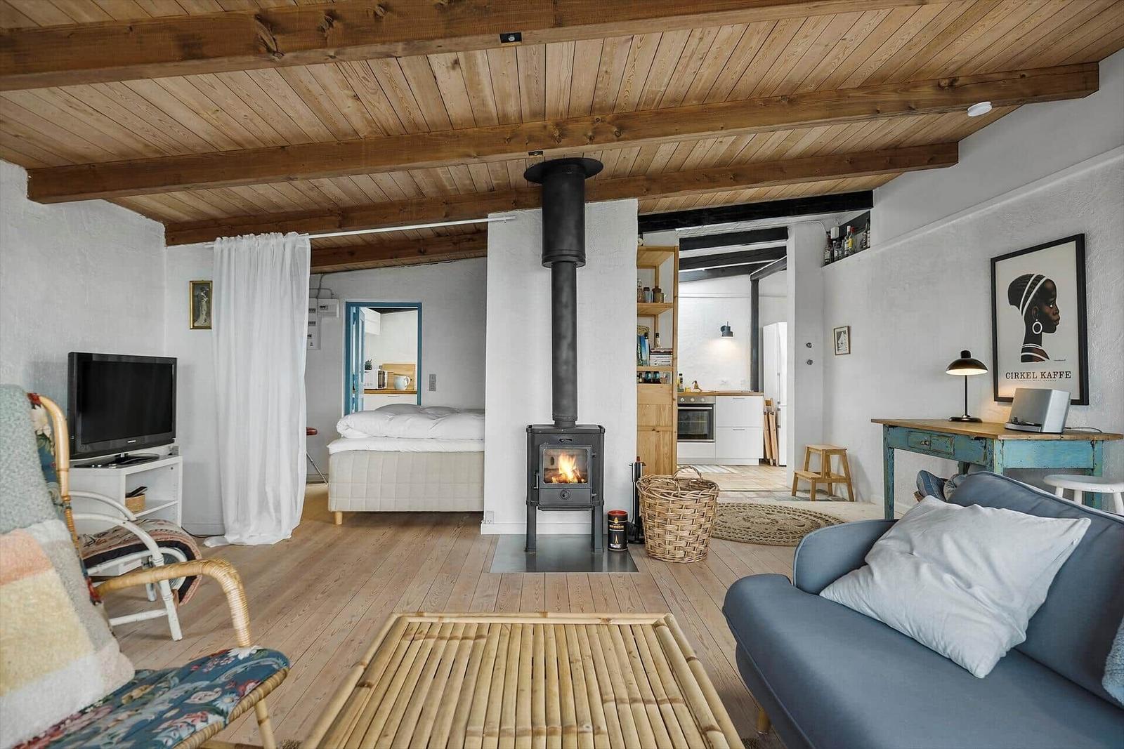 Living space with fireplace, sofa, and bed in background. Wooden ceiling and floor.