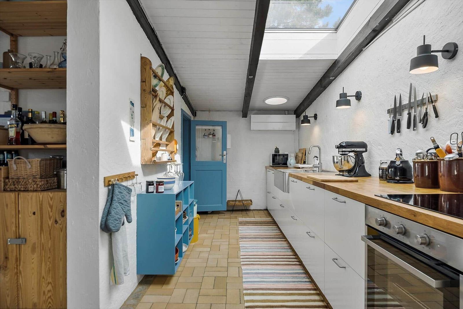 Kitchen with worktop, stove, and kitchen counter. Wooden shelves, blue door, and ceiling beams.