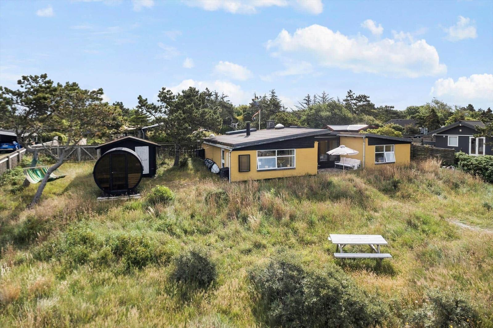 Yellow vacation house with terrace and garden. Adjacent round sauna. Wooden table in the grass.