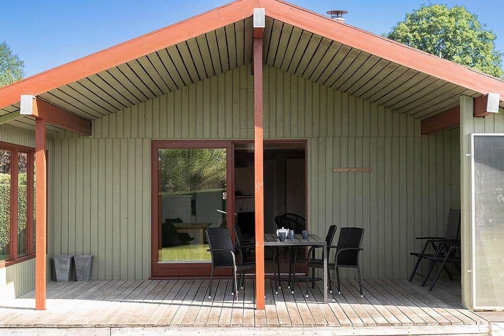 Haus mit Terrasse, Tisch und Stühlen, Glasfront und Holzwand.
