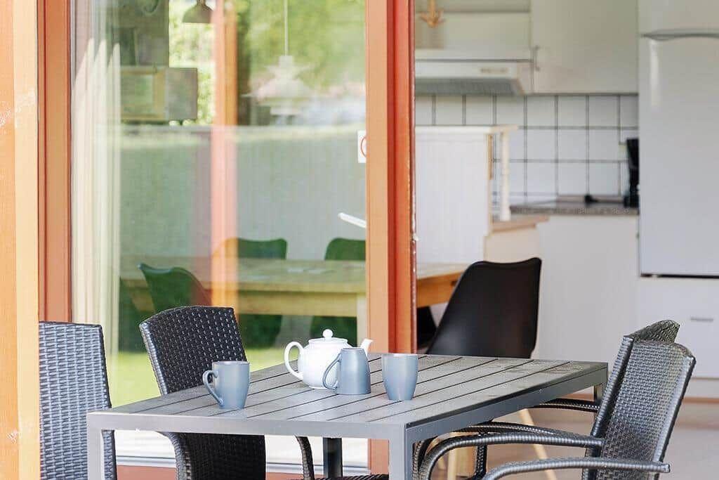 Terrassentisch mit vier Stühlen und Teekanne. Küche im Hintergrund sichtbar.