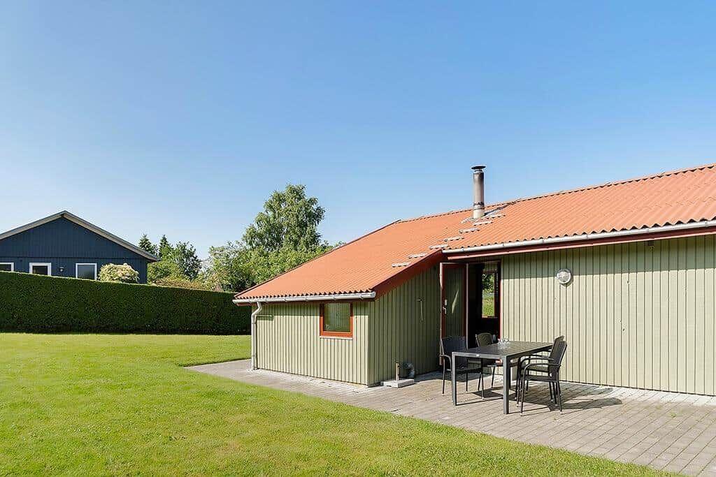 Haus mit Terrasse, Tisch und Stühlen, umgeben von Gras und Bäumen.