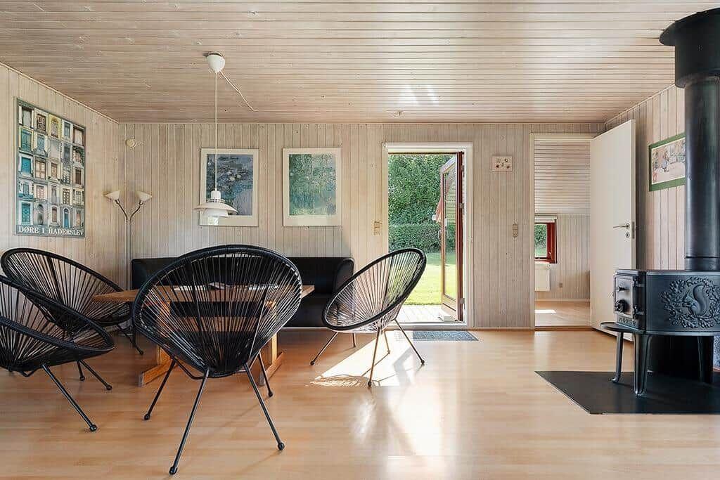Ein Raum mit Holzwandverkleidung, einem Esstisch, drei schwarzen Stühlen und einem Kaminofen.