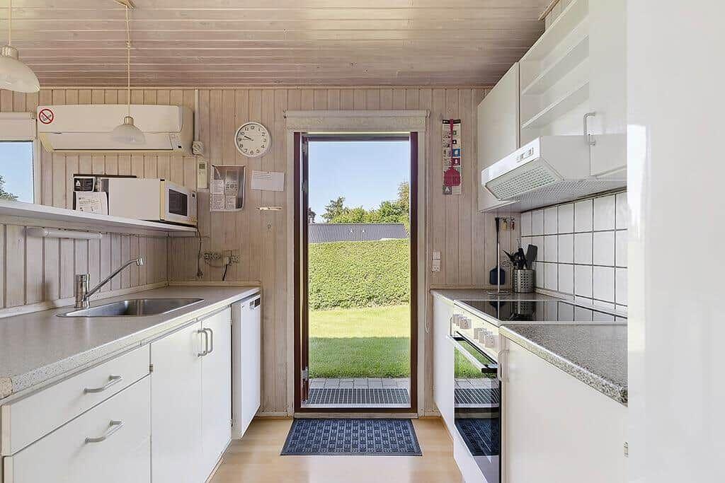 Küche mit Blick auf grünen Garten. Weiße Schränke, Spüle und Herd.