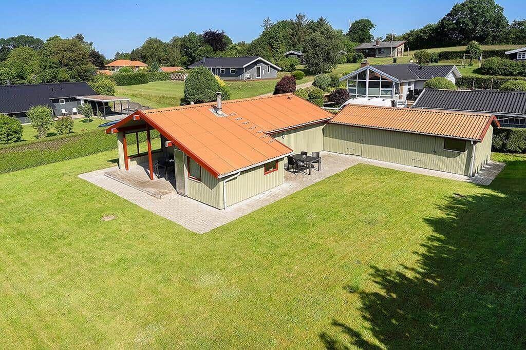 Haus mit orangefarbenem Dach und großem Garten. Terrasse mit Tisch und Stühlen.