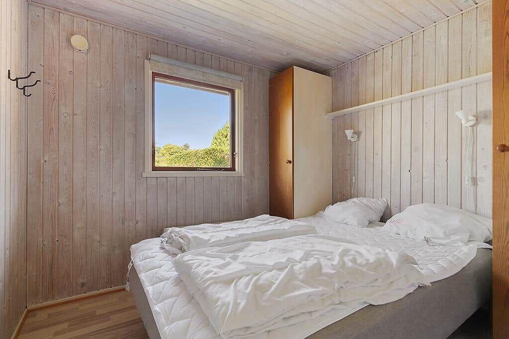 Schlafzimmer mit Holzwand, Bett und Fenster mit Blick auf Bäume.