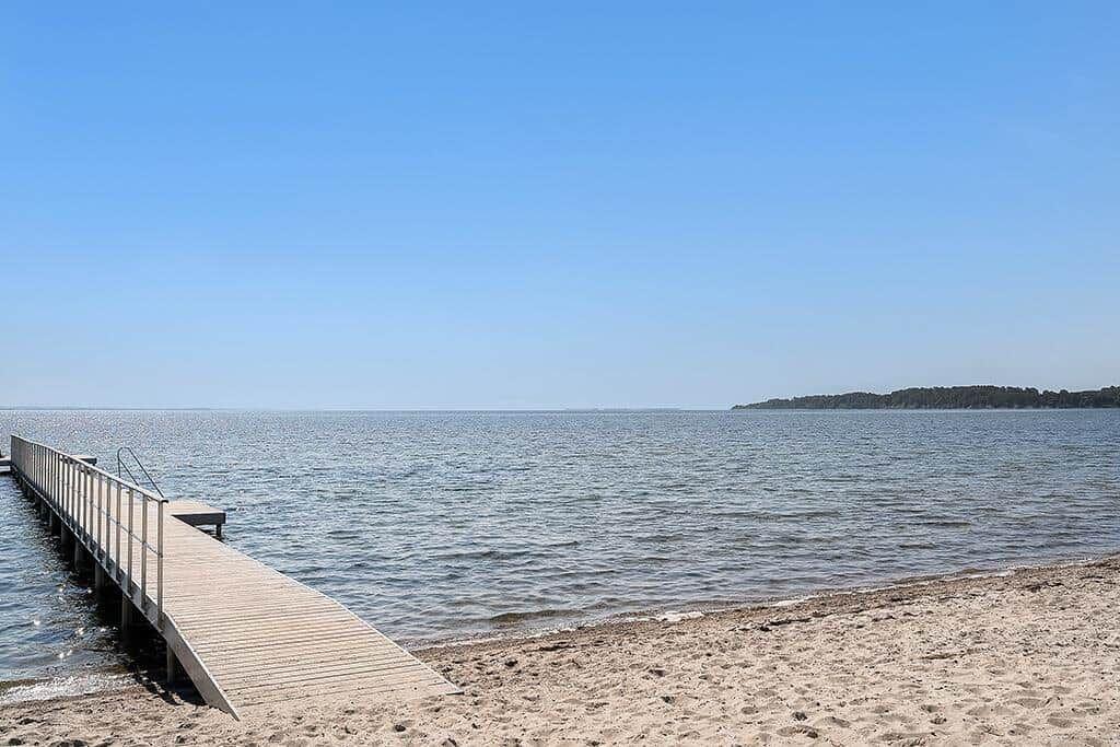 Holzsteg führt zum Wasser. Strand und Horizont sind sichtbar.