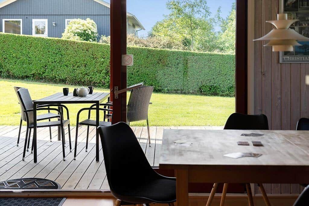 Terrasse mit Tisch und Stühlen, Blick auf grünen Rasen und Hecke.