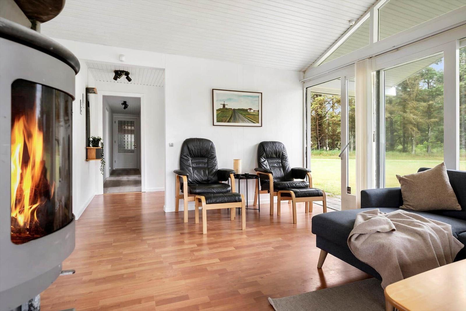 Wohnzimmer mit Kamin, zwei Sessel und Sofa. Blick auf grüne Landschaft.