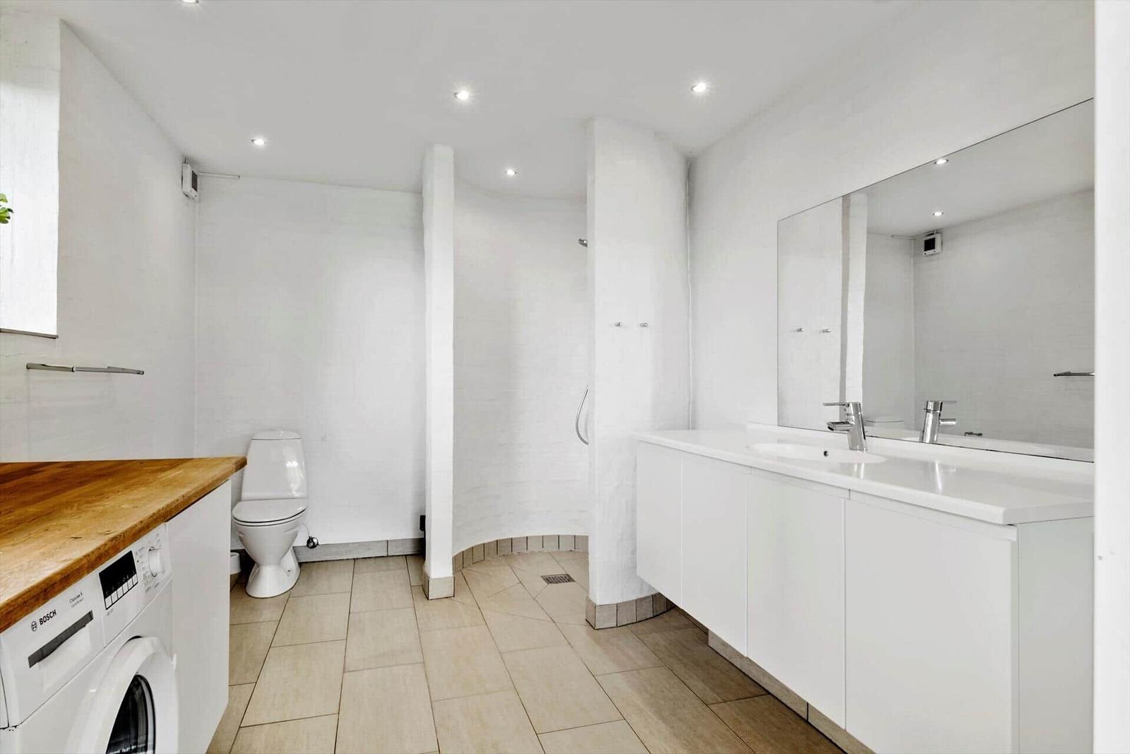 Bathroom with shower, sink, and toilet. Floor tiles and washing machine.
