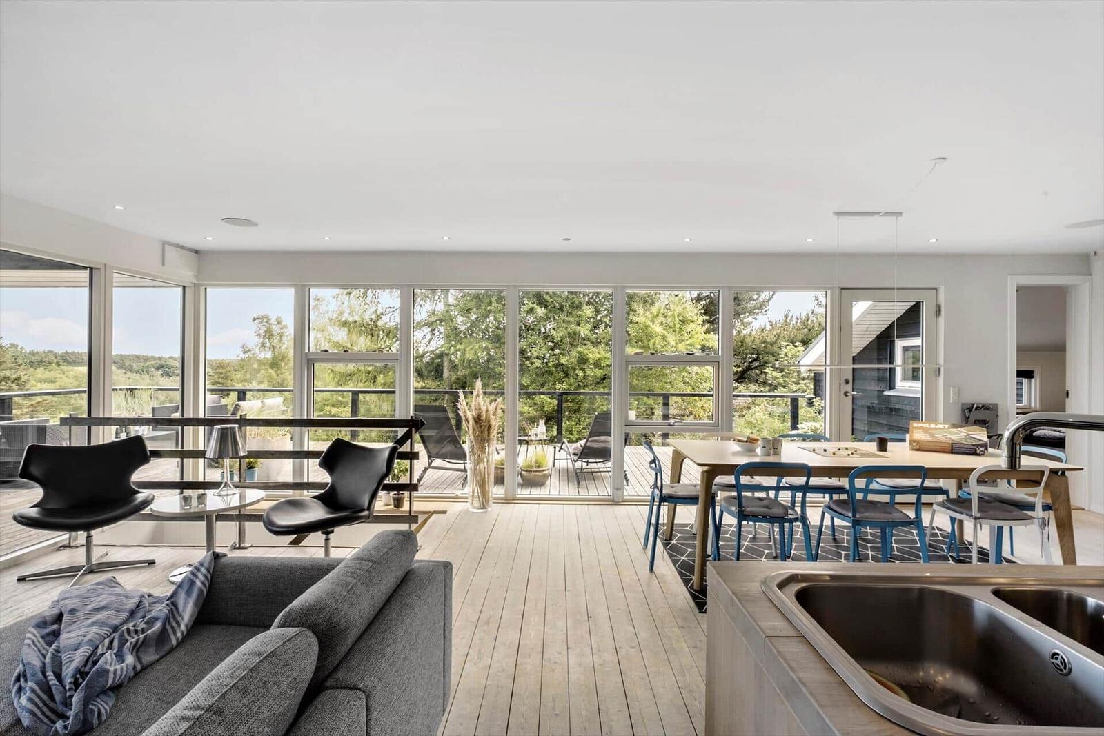 Living and dining area with balcony and wooden floor. Modern furniture and large windows.