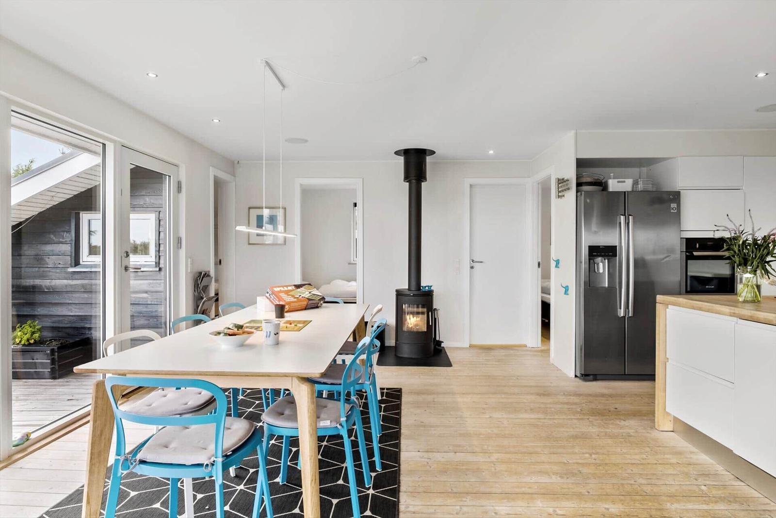 Dining area with table and chairs, wood stove, and kitchen with refrigerator.