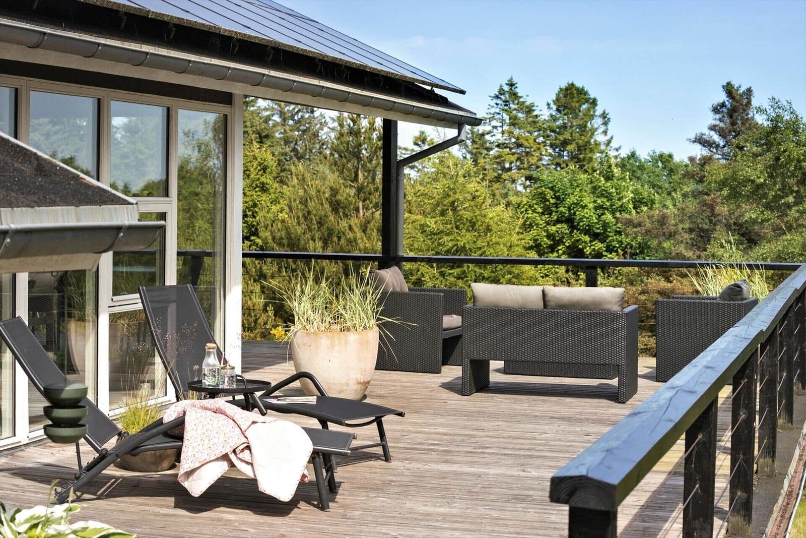 Deck with lounge chairs and seating, surrounded by trees and plants.