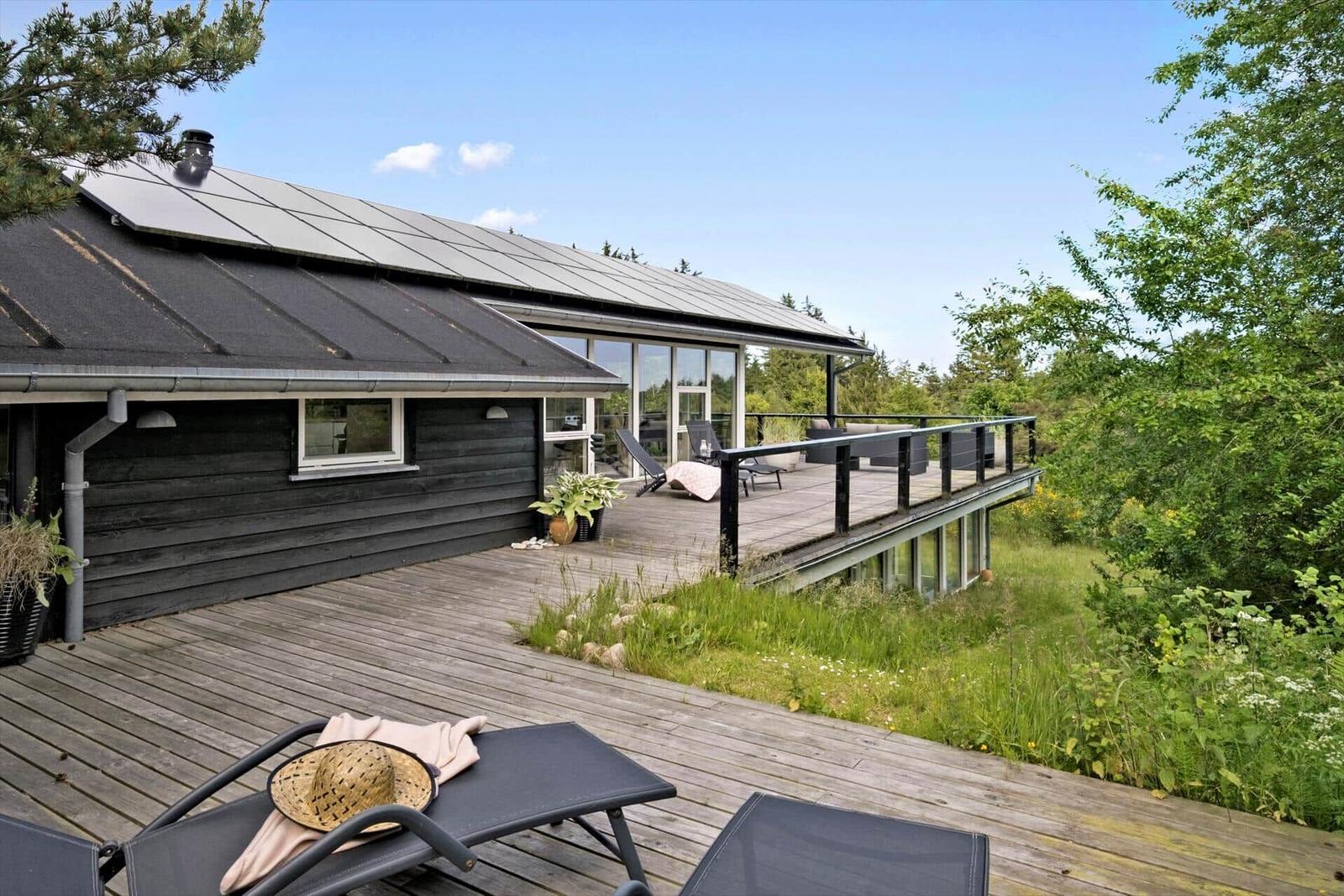 Modern villa with wooden terrace and garden. Solar panels on roof.