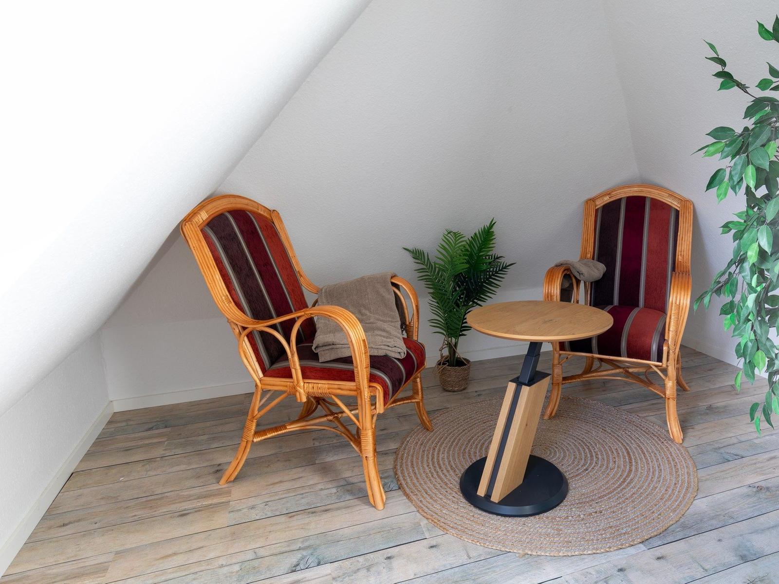 Zwei Rattan-Stühle mit Streifenbezug und runder Tisch auf Teppich.