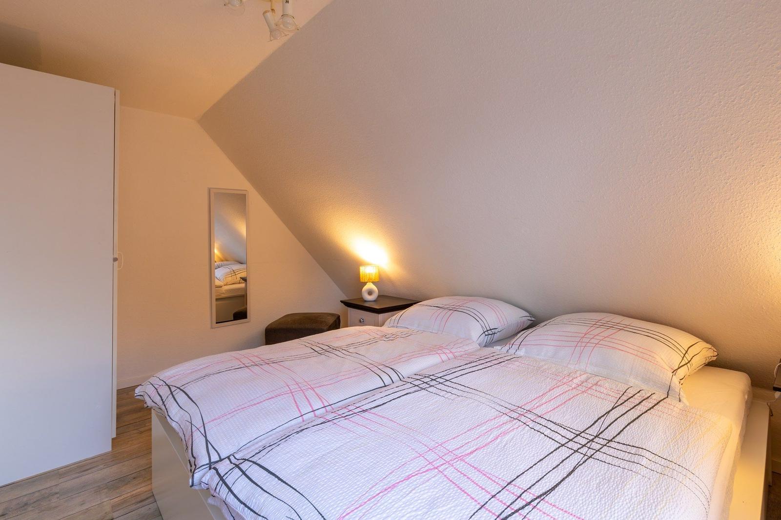 Schlafzimmer mit Doppelbett, Nachttisch und Spiegel an geneigter Wand.