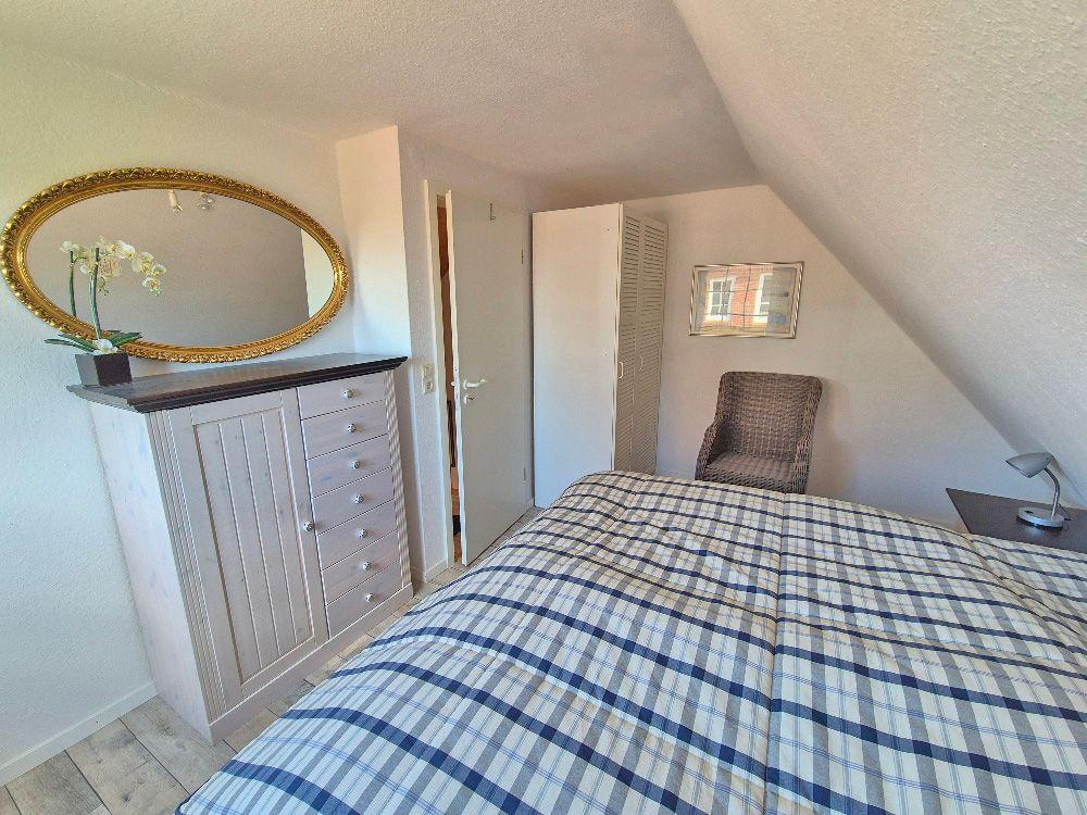 Schlafzimmer mit Bett, Kleiderschrank und Spiegel an der Wand.