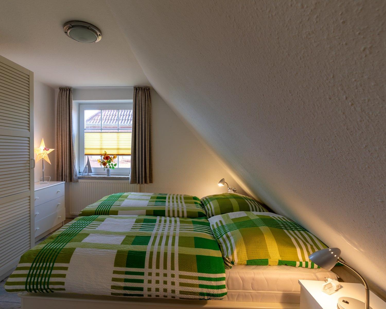 Schlafzimmer mit grün-weißem Bettbezug, Fenster mit Jalousie und Nachttische.