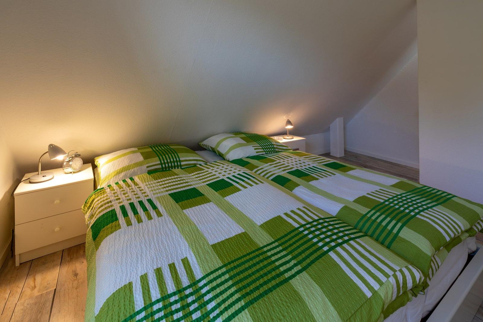 Schlafzimmer mit Doppelbett, grün-weißem Bettzeug und zwei Nachttischen mit Lampen.