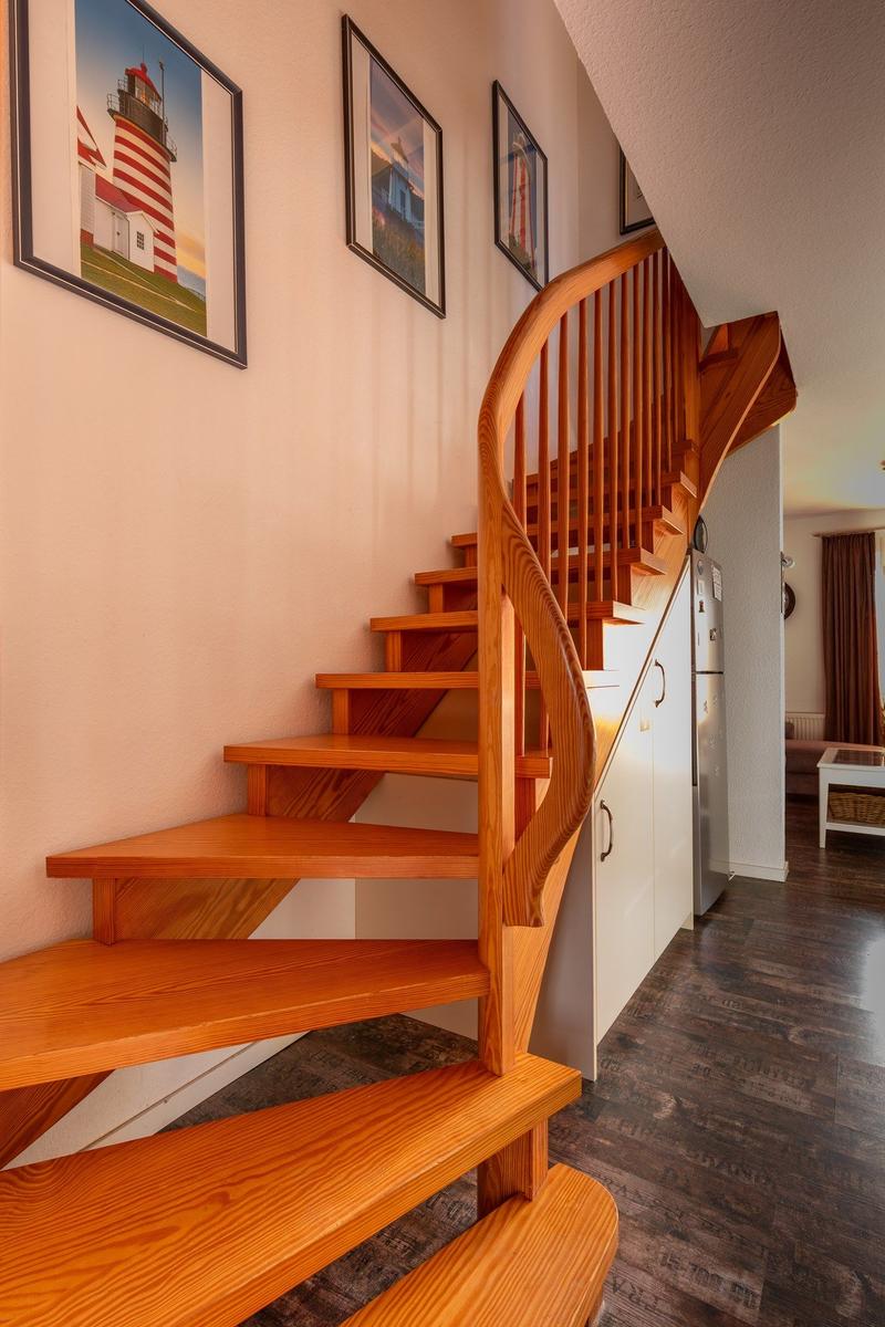 Holztreppe mit Geländer führt nach oben. An der Wand hängen Bilder von Leuchttürmen.
