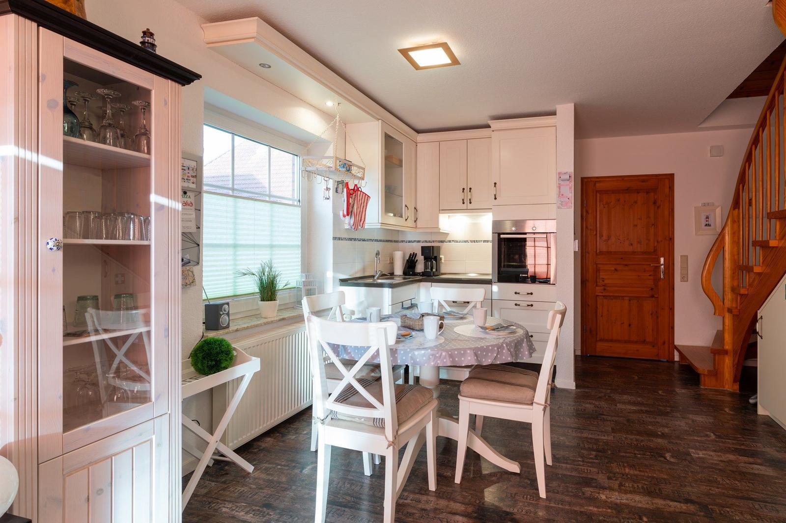 Küche mit Essbereich, Holztreppe und Glasvitrine mit Geschirr.